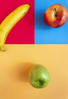 Red apple, green apple and banana on three colors background. Abstract background of fruits with creative design thinking. photo