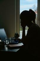 Silhouette of woman working remotely at home office with laptop photo