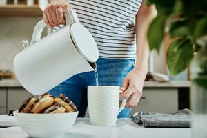 Woman pouring water from kettle for brewing tea photo