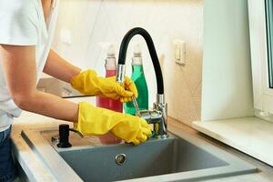 Woman cleaning kitchen sink with water tap photo