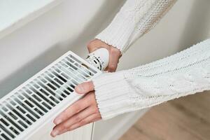 Woman in warm sweater adjusting temperature on heating radiator photo