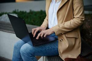 Woman sitting on bench in city street and using laptop photo
