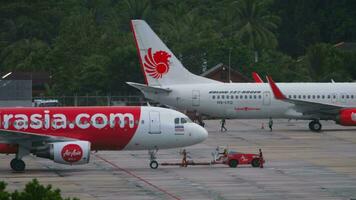 PHUKET, THAILAND NOVEMBER 28, 2019 - Tractor towing Airbus A320 of AirAsia at Phuket airport. Airport on tropical island, airfield and palm trees. Boeing 737 of Thai Lion Air in the background video