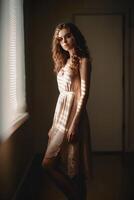 natural portrait of a European young girl in simple rustic clothes standing by the window, natural photo, soft light, art photo