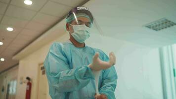 médico o cuidado de la salud trabajador caminar en un personal protector equipo preparando y vistiendo mano guantes en el interior hospital o clínica preparar en medio de coronavirus o covid-19 epidemia o pandemia. video