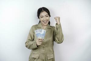 A successful young government worker woman is wearing khaki uniform holding cash money in Indonesian rupiah isolated by white background photo