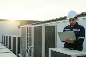 Asian maintenance engineer works on the roof of factory. contractor inspect compressor system and plans installation of air condition systems in construction. technology, online, mobile application. photo