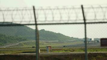 A passenger plane is taxiing after landing in Phuket. View of the runway through the fence. Airport traffic video