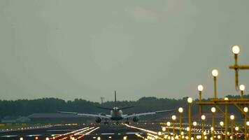 posterior vista, el avión Taxis a el terminal después aterrizaje. cinematográfico imágenes de aterrizaje luces y un avión de línea pista. iluminado aeródromo video