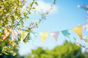 Colorful pennant string decoration in green tree foliage against blue sky summer party background with space for text photo