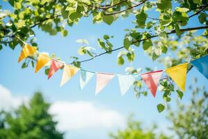 Colorful pennant string decoration in green tree foliage against blue sky summer party background with space for text photo