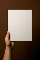 A human hand holding a blank sheet of white paper or card isolated on brown background. ai generated photo