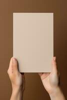 A human hand holding a blank sheet of white paper or card isolated on brown background. ai generated photo