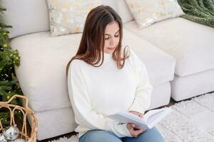 mujer en calentar blanco invierno suéter sentado en sofá leyendo un libro foto
