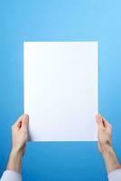 A human hand holding a blank sheet of white paper or card isolated on blue background. ai generated photo