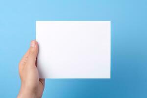 A human hand holding a blank sheet of white paper or card isolated on blue background. ai generated photo