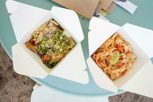 Asian noodles with vegetables and spices in paper boxes, eating outside photo