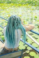 joven mujer con hermosa azul rastas descansando en loto lago foto