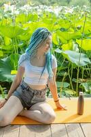 joven mujer con hermosa azul rastas descansando en yoga estera en loto lago foto