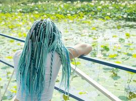 joven mujer con hermosa azul rastas descansando en loto lago foto