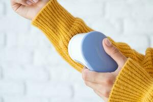 woman in yellow sweater using fabric pills removing tool photo