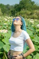 joven mujer con hermosa azul rastas descansando en loto lago foto