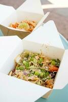 asiático tallarines con vegetales y especias en papel cajas, comiendo fuera de foto