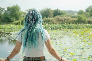 joven mujer con hermosa azul rastas descansando en loto lago foto