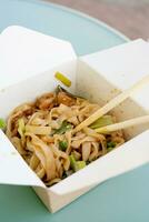 Asian noodles with vegetables and spices in paper boxes, eating outside photo