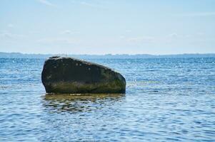 Single stone, rock in the Baltic Sea in sunshine. Landscape photo from coast.