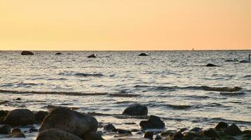 atardecer, Roca playa con pequeño y grande rocas en frente de el iluminado mar. foto