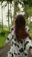 Vertikale Video ein jung Mädchen im ein Kleid läuft unter Palme Bäume