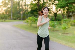 Fit Asian young woman jogging in park smiling happy running and enjoying a healthy outdoor lifestyle. Female jogger. Fitness runner girl in public park. healthy lifestyle and wellness being concept photo