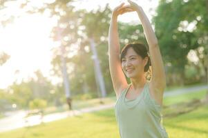 Female jogger. Fit young Asian woman with green sportswear stretching muscle in park before running and enjoying a healthy outdoor. Fitness runner girl in public park. Wellness being concept photo