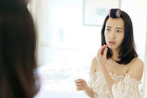 Beautiful young Asian woman applying makeup in front of the mirror. Lifestyle people concept. Advertisement for skin cream, anti-wrinkle cream, baby face photo