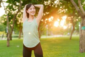 hembra persona que practica jogging. ajuste joven asiático mujer con verde ropa de deporte extensión músculo en parque antes de corriendo y disfrutando un sano exterior. aptitud corredor niña en público parque. bienestar siendo concepto foto