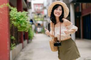 Happy youth asian woman with camera travels street city trip on leisure weekend. Young hipster female tourist sightseeing summer urban Bangkok destination. Asia summer tourism concept. photo