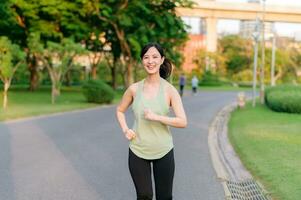 Fit Asian young woman jogging in park smiling happy running and enjoying a healthy outdoor lifestyle. Female jogger. Fitness runner girl in public park. healthy lifestyle and wellness being concept photo