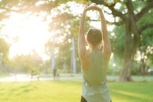 Female jogger. Fit young Asian woman with green sportswear stretching muscle in park before running and enjoying a healthy outdoor. Fitness runner girl in public park. Wellness being concept photo