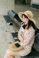 young asian woman traveler with weaving basket waiting for train in train station. Journey trip lifestyle, world travel explorer or Asia summer tourism concept. photo