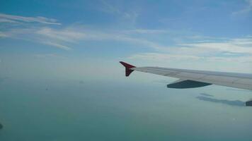 Airplane is flying in the sky over the blue ocean. Closeup view on the wing from the jet which is moving in aerospace. Spending vacation in the trip video