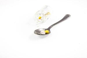 glass container and a silver spoon with medicine on a white isolated background photo