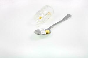 glass container and a silver spoon with medicine on a white isolated background photo