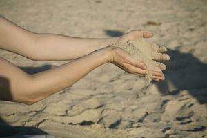 de cerca de manos con arena que cae en un playa foto