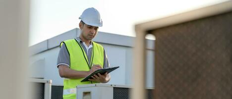Asian maintenance engineer works on the roof of factory. contractor inspect compressor system and plans installation of air condition systems in construction. Checklist, inspector, control photo