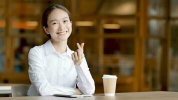 asiatico donna seduta su tavolo nel davanti di caffè passaggio mini cuore per telecamera video