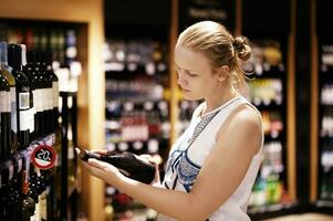 Woman reading inscription on the wine bottle in store photo