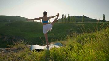 atlético mujer haciendo yoga poses en parte superior de un montaña durante puesta de sol. Deportes niña trenes y lo hace extensión ejercicios en el montañas. sano estilo de vida, zenismo, rutina de ejercicio concepto. lento movimiento. video