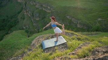 atlético mujer haciendo yoga poses en parte superior de un montaña durante puesta de sol. Deportes niña trenes y lo hace extensión ejercicios en el montañas. sano estilo de vida, zenismo, rutina de ejercicio concepto. lento movimiento. video