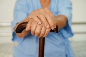 Asian elderly disability woman patient holding walking stick in wrinkled hand at hospital. photo